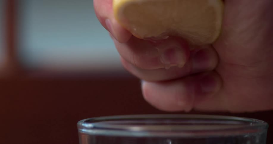 A hand squeezes a lemon into a glass