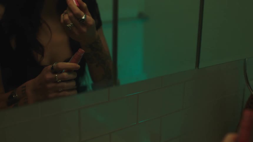 Woman applying lip gloss to her lips in front of the mirror