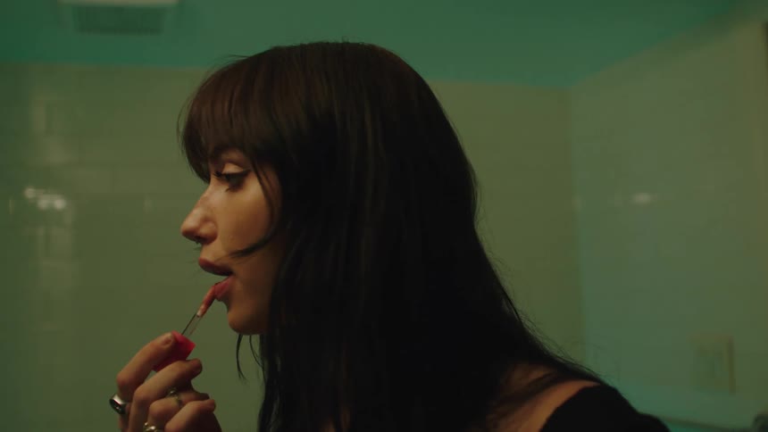 A young woman with long brown hair applies makeup while in the bathroom