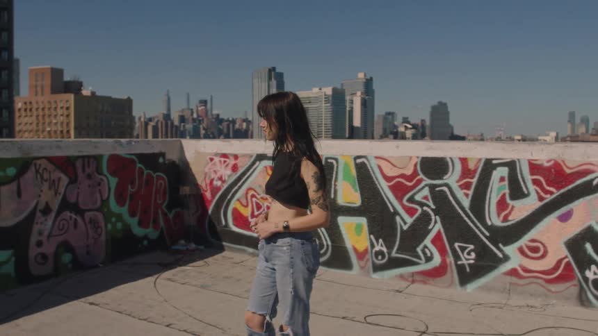 Woman walks on graffiti decorated roof and looks at nearby skyscrapers