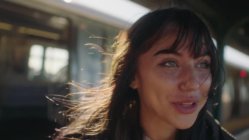 A lady wearing a nose ring is laughing while talking as she stand beside a train