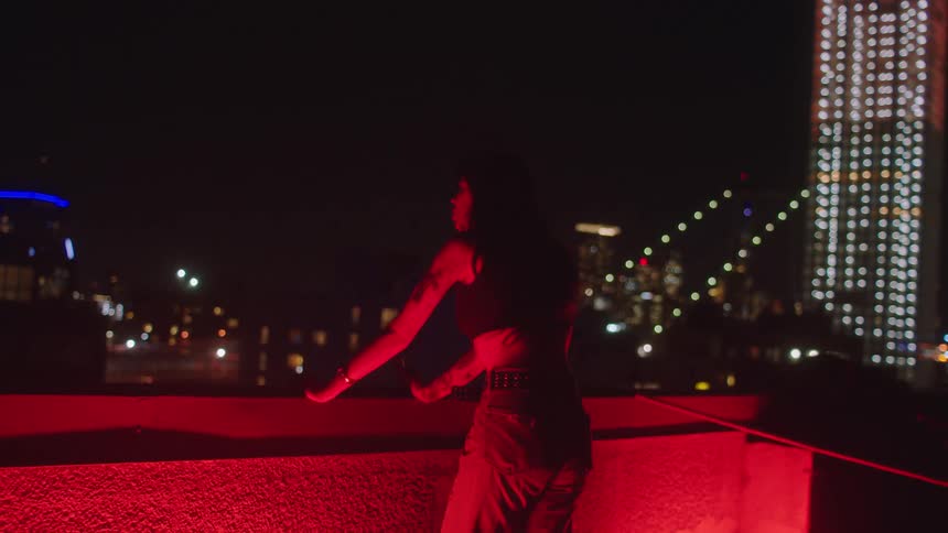 Woman observing the view of a metropolis at night with a red reflective light beneath her