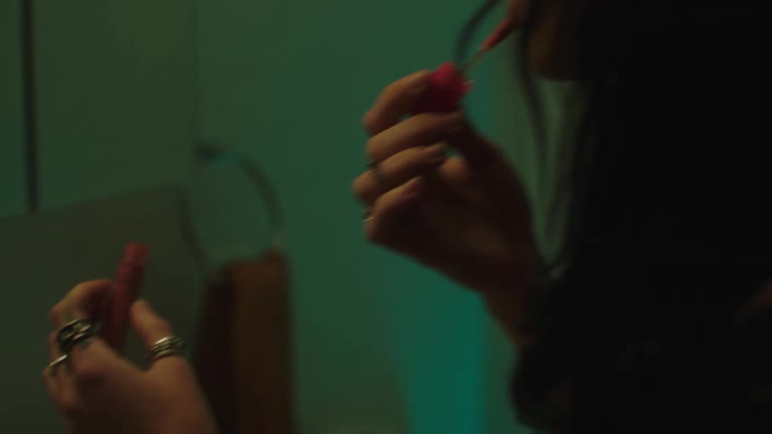 Woman applying lip gloss to her lips in front of the mirror