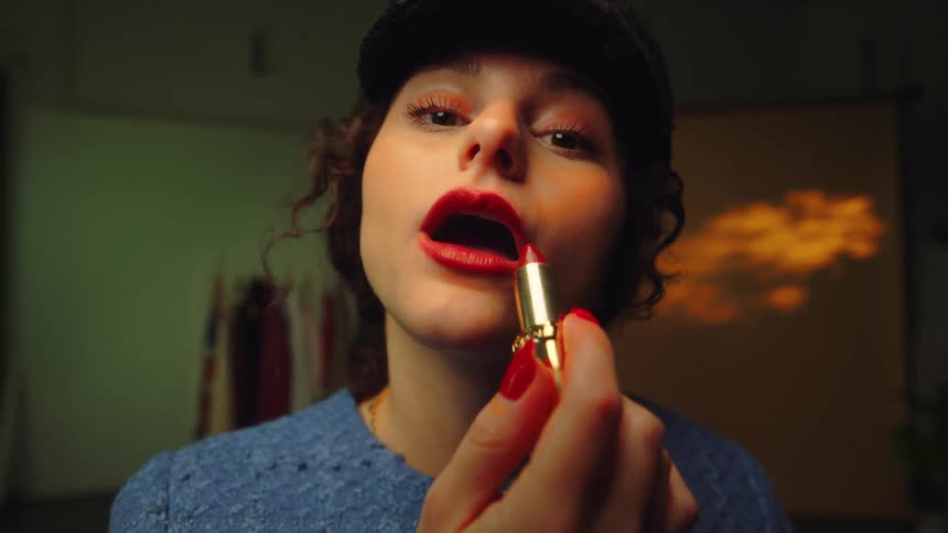 A young woman applying red lipstick to her lips