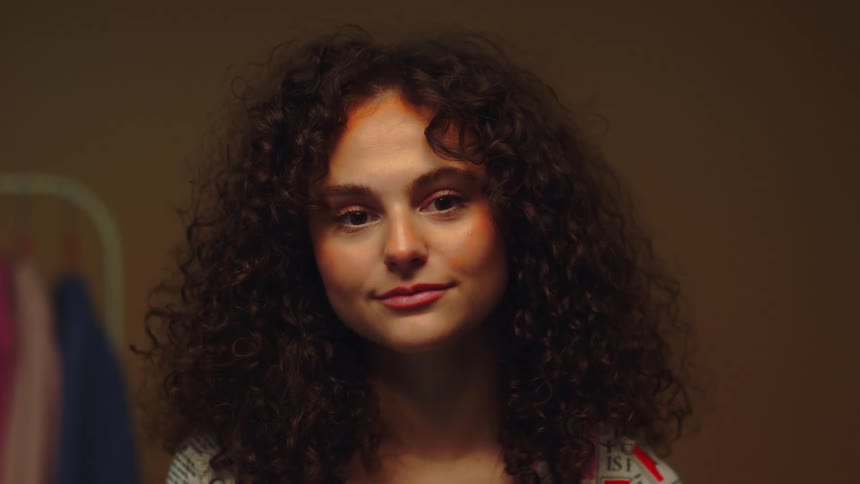 A woman with curly brown hair poses and smiles brightly