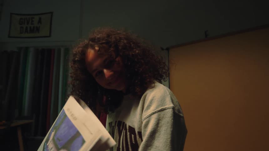 Lady holds a printed newspaper smiling while seated in a room