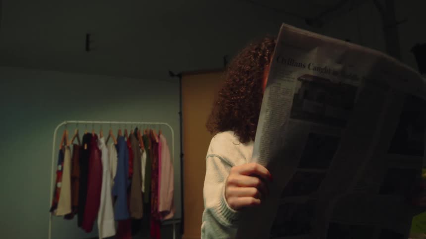 Young woman sitting reading a newspaper and covering her face