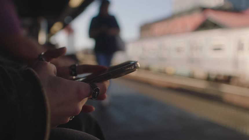 A womans hand checking a smart phone while sitting at a train station