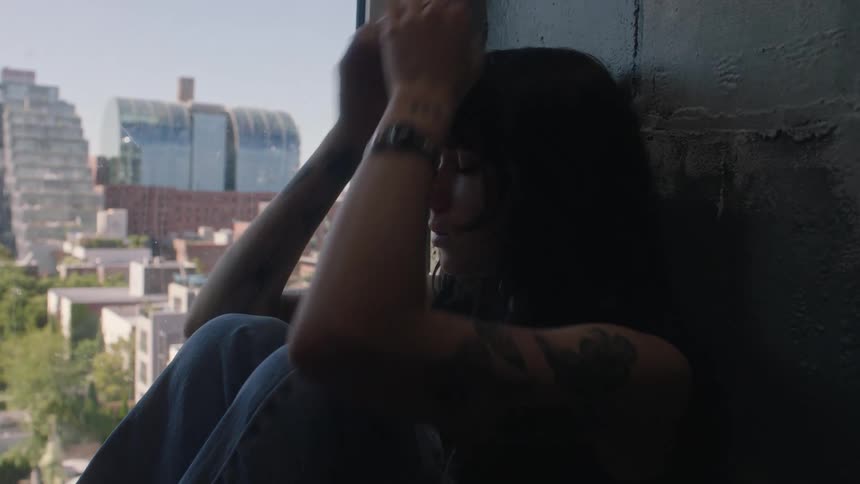 Young woman sitting and leaning against the wall placing her hands on her head in a sign of sadness