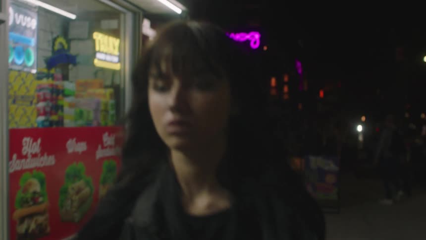 A woman is walking on a sidewalk at night in a suburban neighborhood with a small grocery store