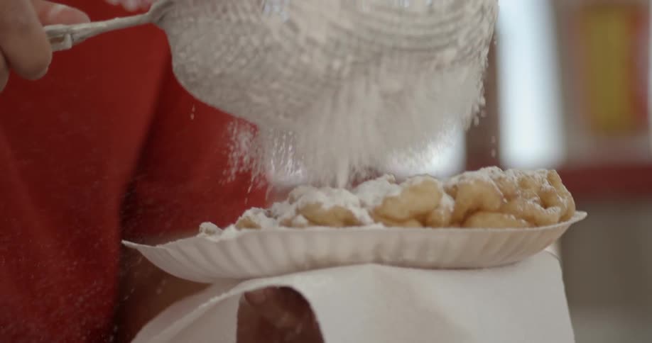 Person sprinkling powdered sugar on funnel cake
