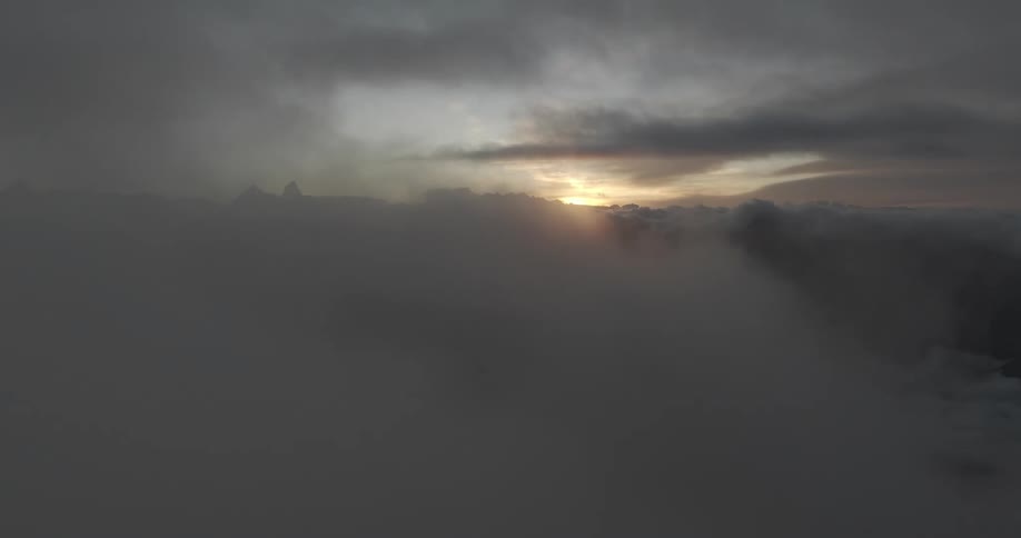 Aerial panorama above the clouds over the mountains with the sun rising on the horizon
