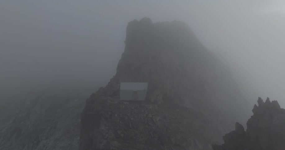 A small building is built into the side of a tall rocky peak on a foggy day