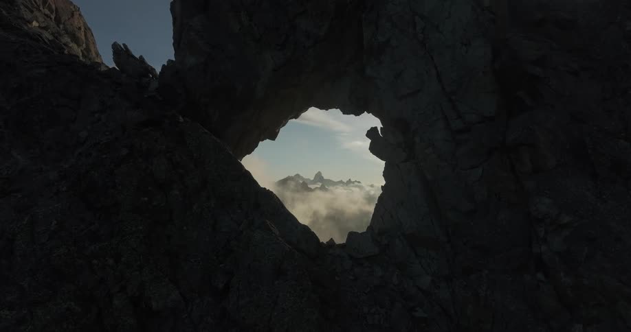 View of a hole in the midst of a mountain with a glimpse of a natural landscape beneath the clouds