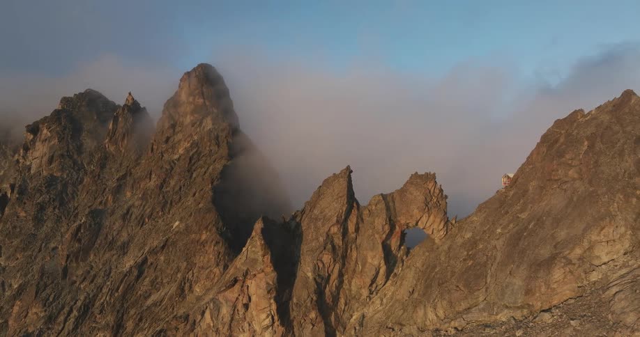 Aerial of a cabin on top of a rocky mountain at dawn