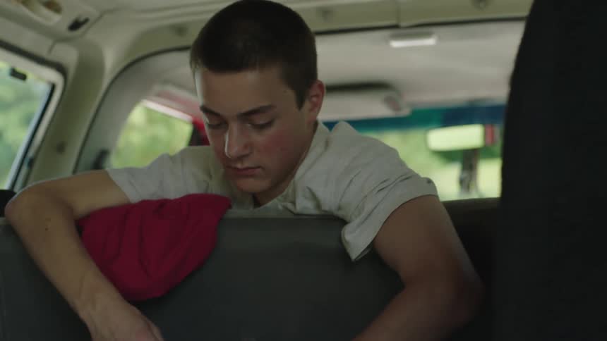 Young man holding foliage for two rabbits in a cage in the trunk of a car