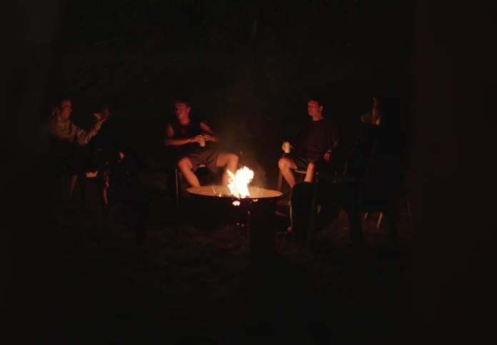 Friends in a circle with a bonfire in the center chatting at night