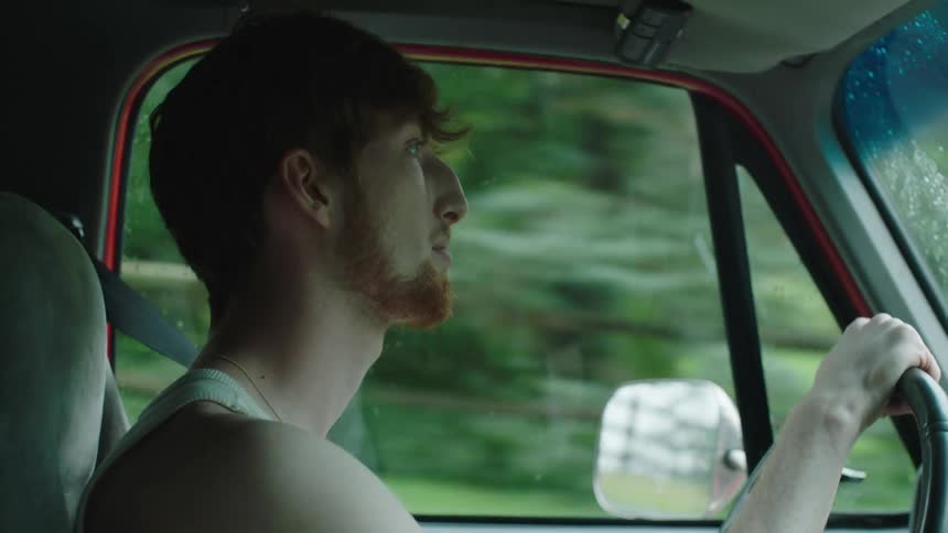 Bearded man with a white undershirt drives a pickup truck in the countryside
