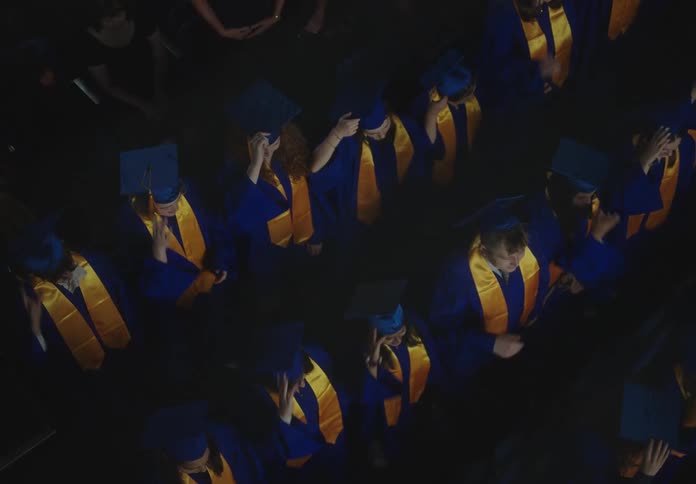 Top view of graduates in gowns standing up tossing their hats in the air and celebrating