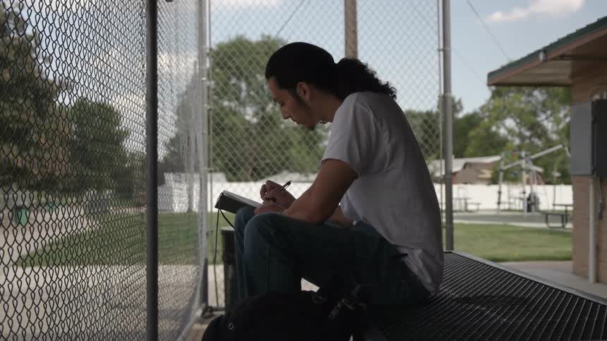 Man sits on a picnic table and writes in a notebook