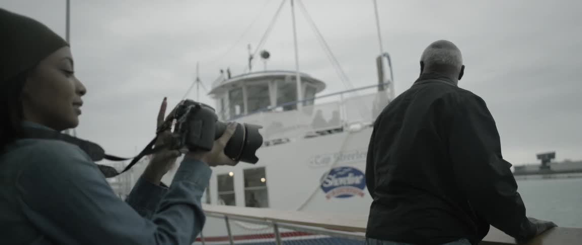 A woman takes photographs of a man greeting a docking ship