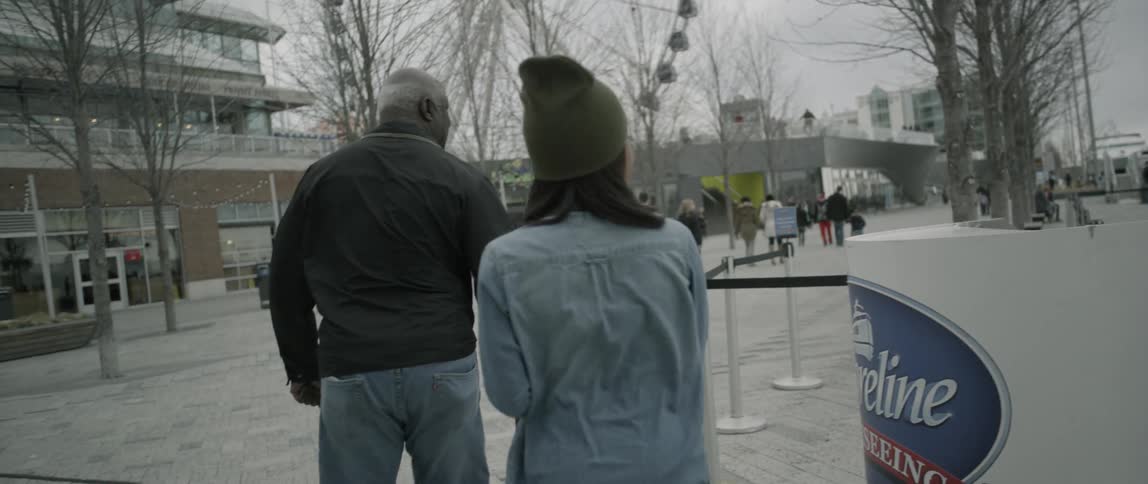 A woman holding a camera follows a man and then turns around
