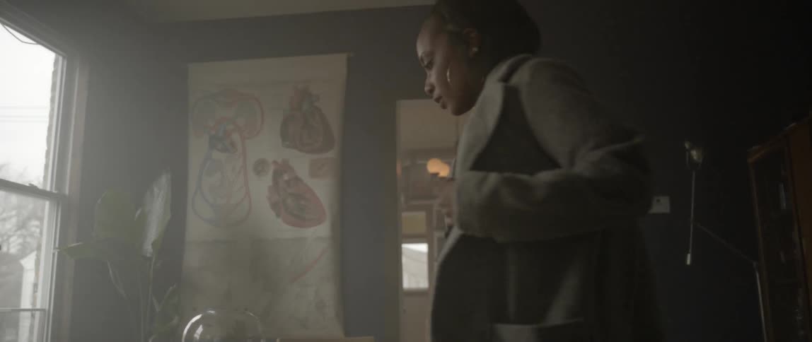 A woman walks into a room and puts on her coat and sits down