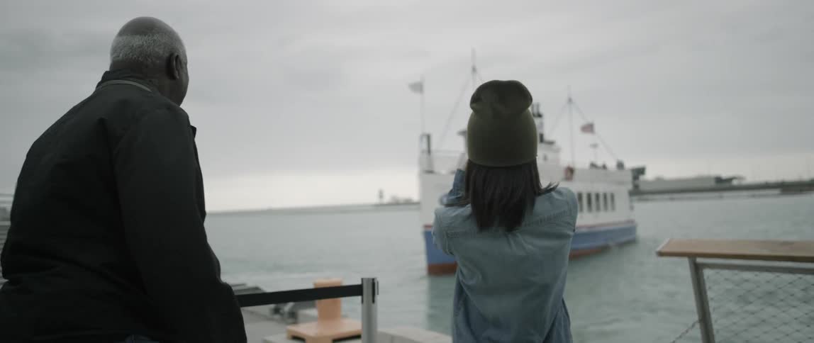 A woman stands with a man and takes photographs of a departing ship