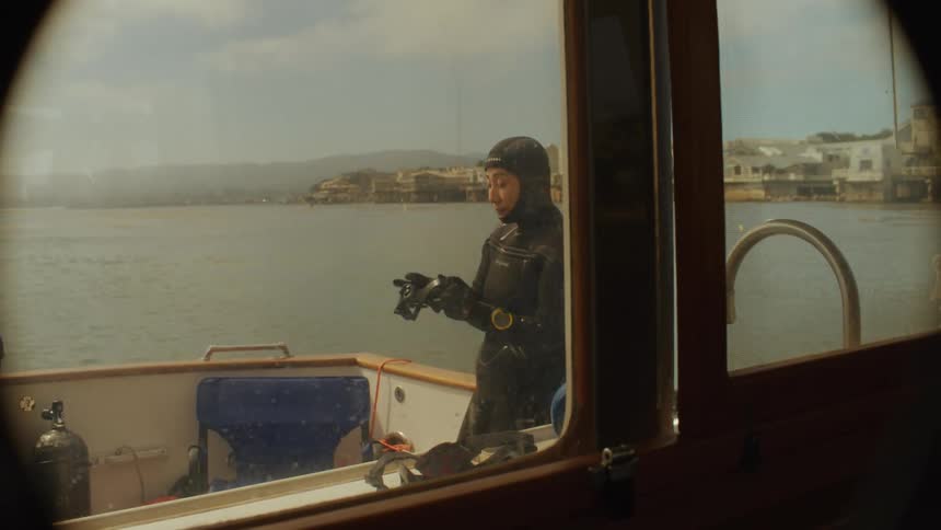 Woman dressed in diving gear on a boat in the water cleaning her diving goggles
