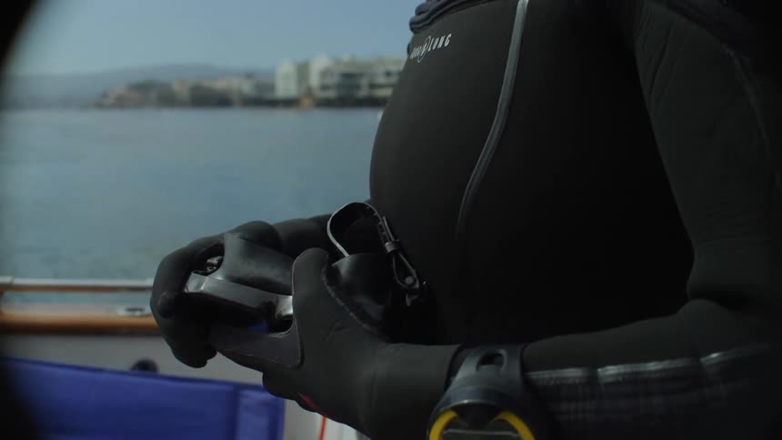 Woman wearing diving gear on a boat outdoors near to the coast with a city and mountains in the background during day time