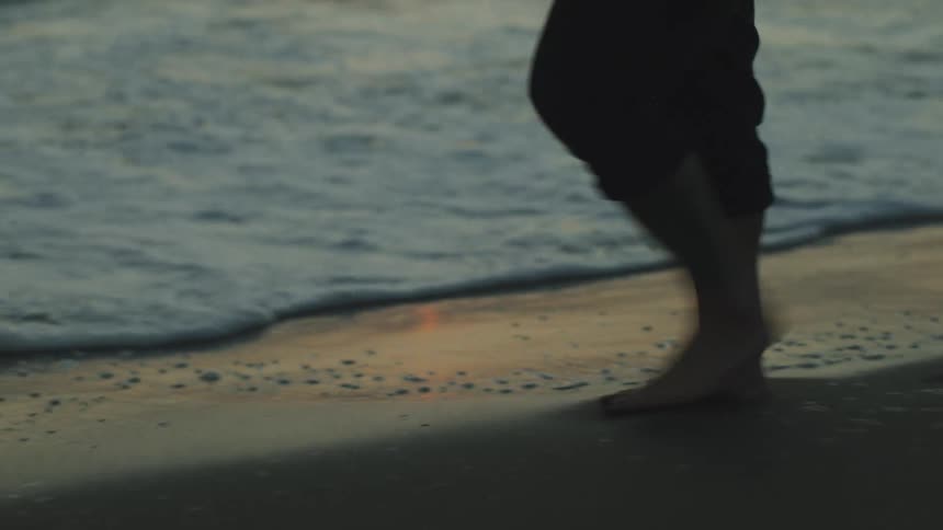 Woman walks across a beach with the sand reflecting the sun at sunset