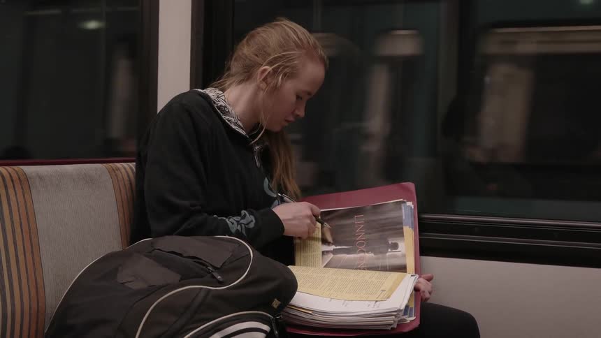 A girl does homework on a subway train