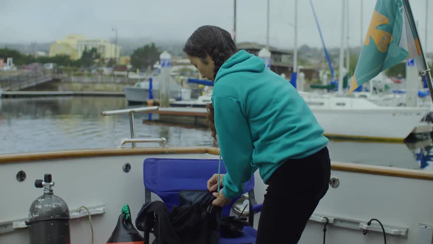 Woman standing on deck of moving boat puts items into a bag