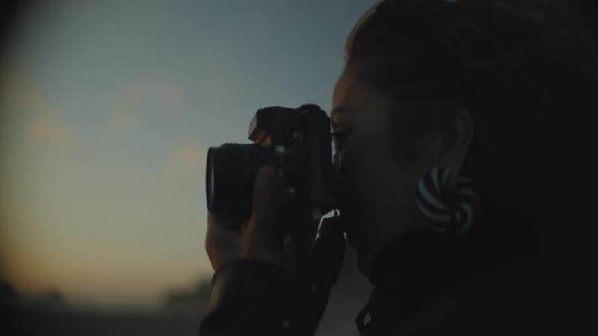 Portrait of a woman taking a photograph with a professional camera in a morning sky