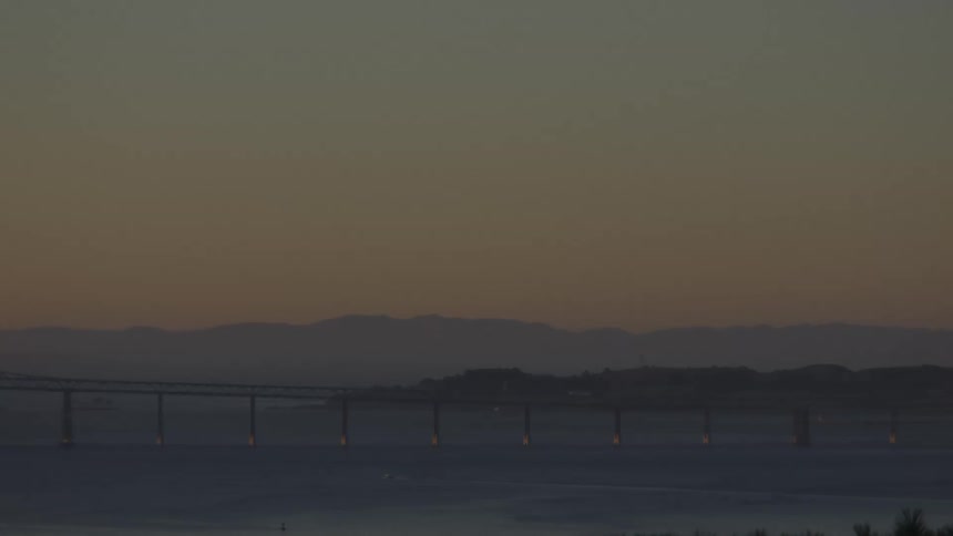 View of the sea with a long bridge and a chain of mountains on the horizon under an orange dawn sky in San Francisco
