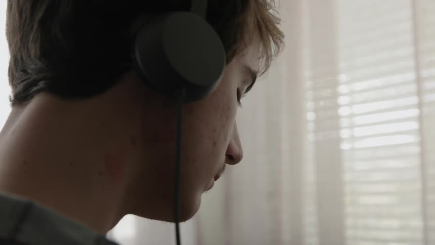 A teenager stands in a room wearing headphones
