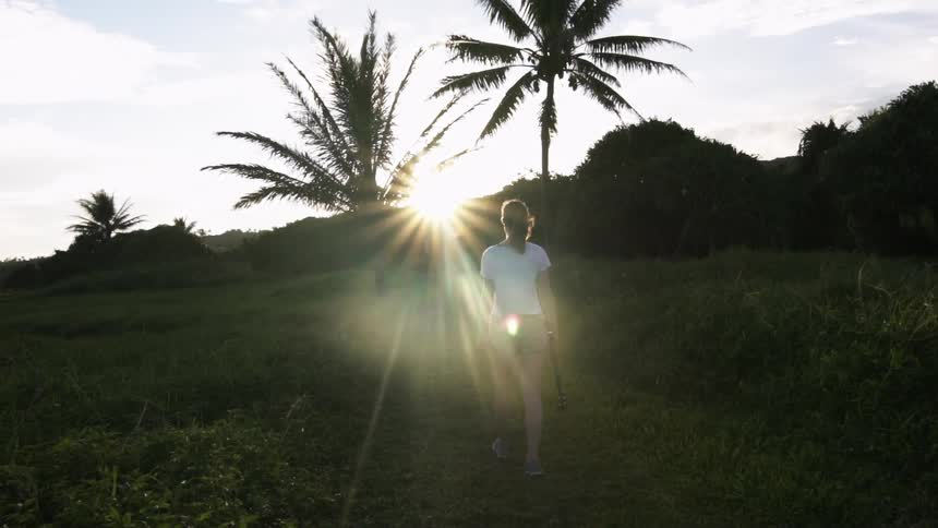 A woman walks up a grassy hill towards the sunset