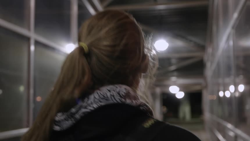 A woman is walking down a glass hall at night
