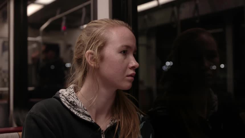 A woman looks out the window of a train at night