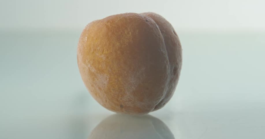 An apricot atop a reflective surface progressively freezes over