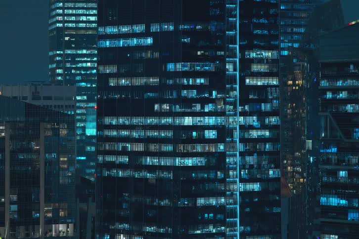 A clip of apartments with electricity and window lights turning on in various skyscrapers