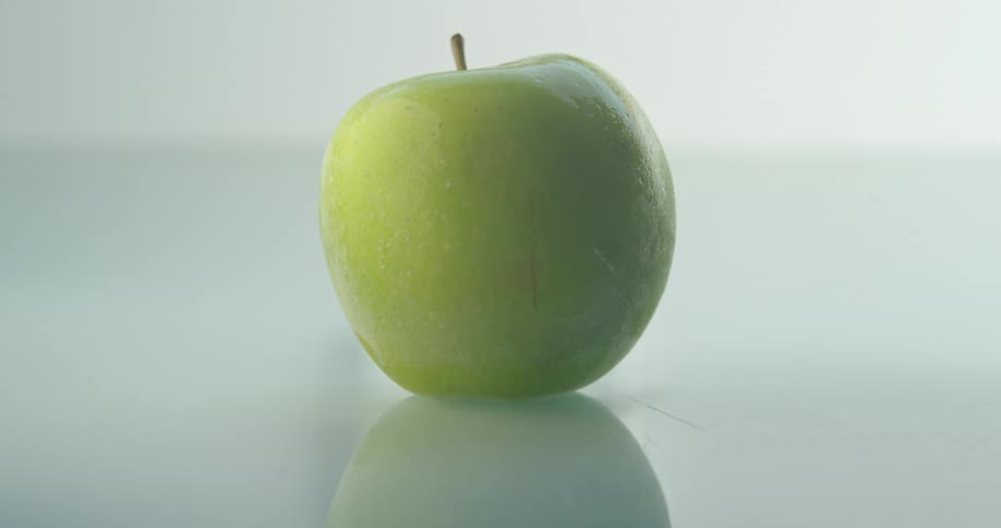 A single green apple on a smooth, reflective surface, rapidly freezes over