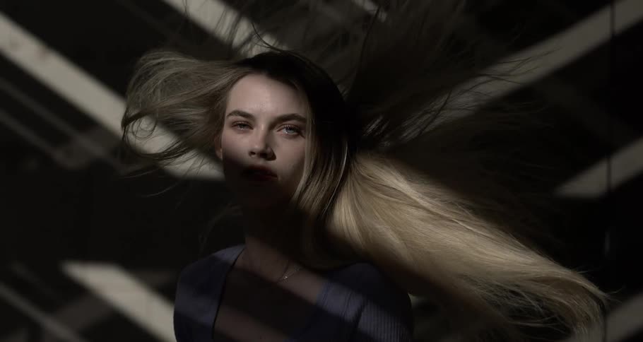 Light beam shines onto woman moving across patterned background with her hair blowing through the air