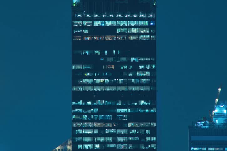View of a building in the midst of a metropolis in a night time lapse with lights turning off and moving