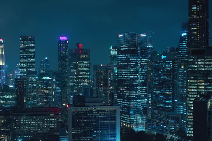 Blue reflected lights turning on and off in windows across the city skyline at night against a dark blue sky