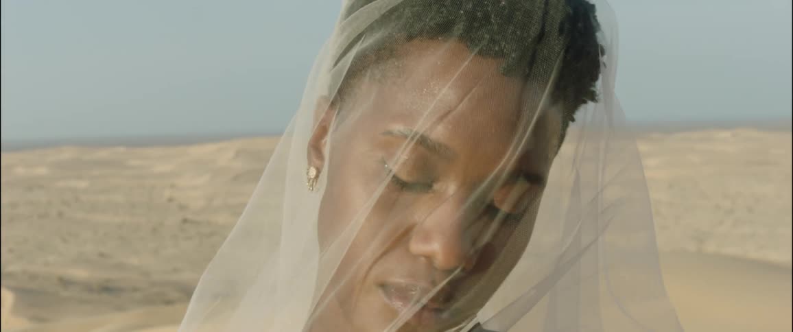 Black female standing in the dessert at midday with white veil covering her face