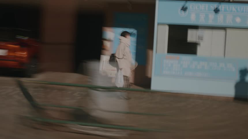 Person wearing an overcoat and carrying a bag walking on the sidewalk of an urban area during day time