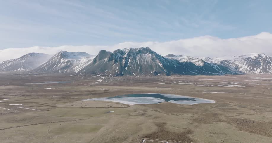 Aerial view of a central lake surrounded by a grassland with a chain of snowcovered mountains on the horizon