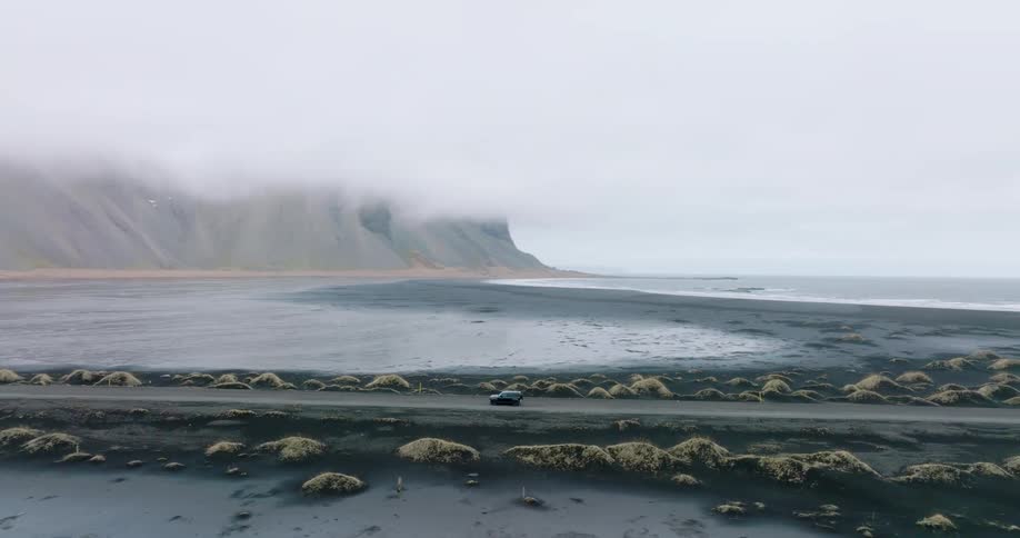 Vehicle parks on dirt road through frozen tundra near seaside cliffs