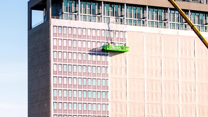 Two men on a moveable platform peel paper off windows of a tall high rise building in a time lapse